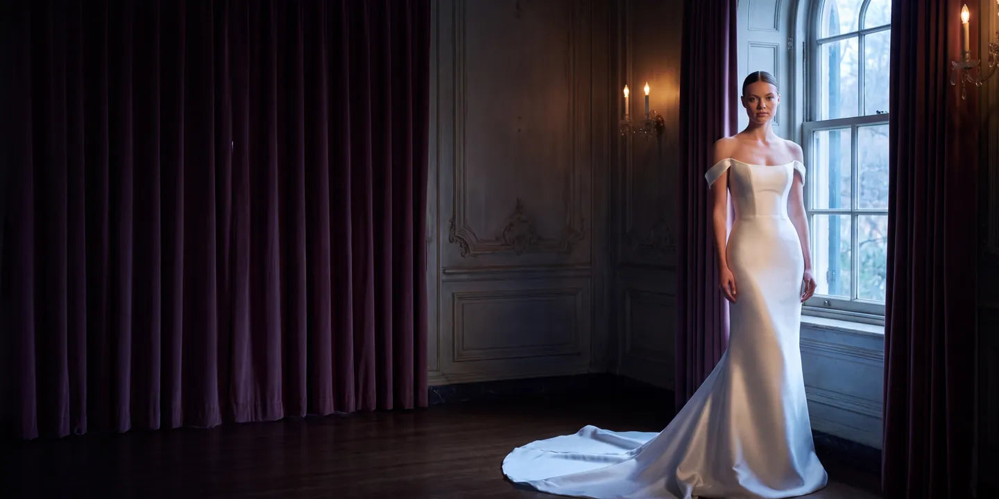 Novia con vestido de satín junto a una ventana en un salón antiguo
